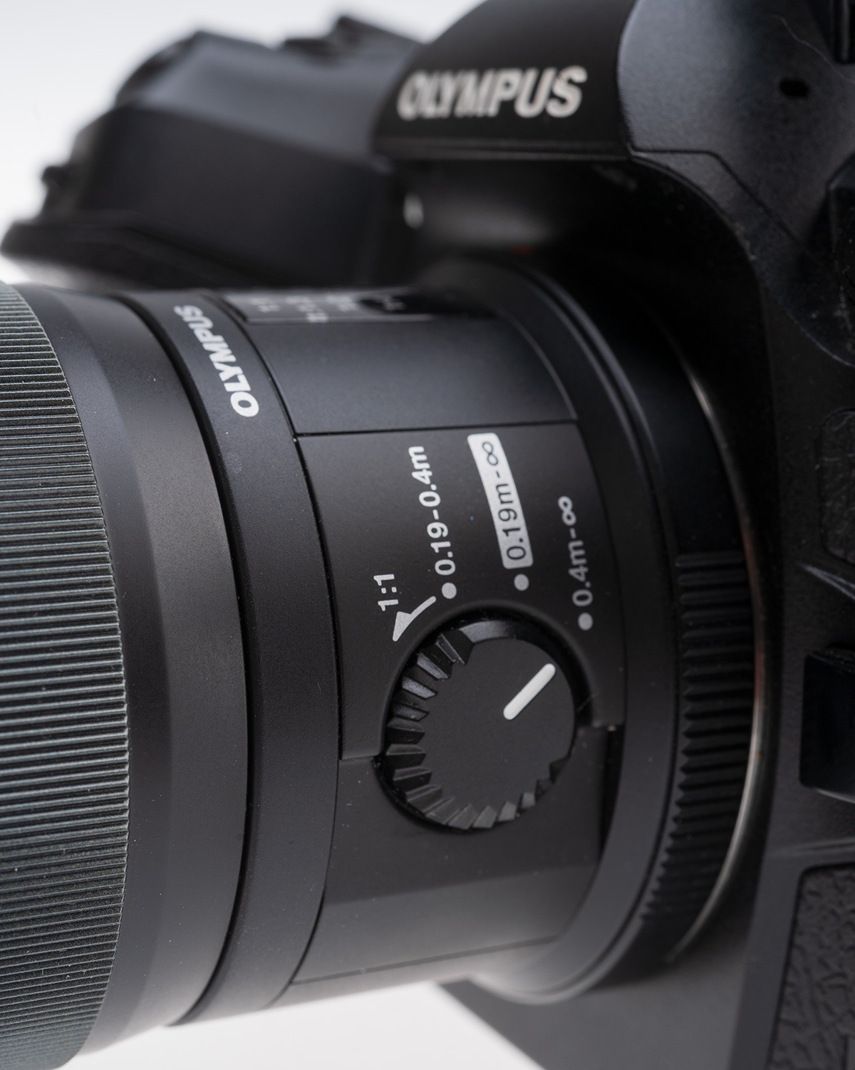 The focus range limiter switch on the left of the 60mm f/2.8 M.Zuiko Macro lens, showing settings for 0.4-infinity, 0.19-infinity, and 0.19-0.4m and fixed 1:1 magnification (move subject or camera, not focus).